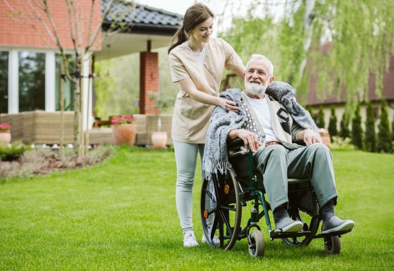 Senior man with helpful volunteer in the garden of professional care home